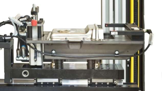 zeigt den auf dem Pressentisch installierten Schiebetisch mit Werkstückaufnahme zum Einschieben der zu clinchenden, aus zwei Hälften bestehenden Elektronikbox aus Aluminium 